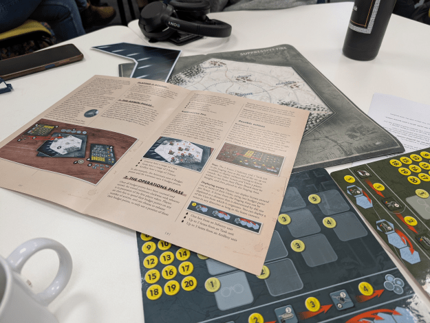 A photo of the Suppressive Fire game, with game board, rulebook, and playing assets. It has a military style.