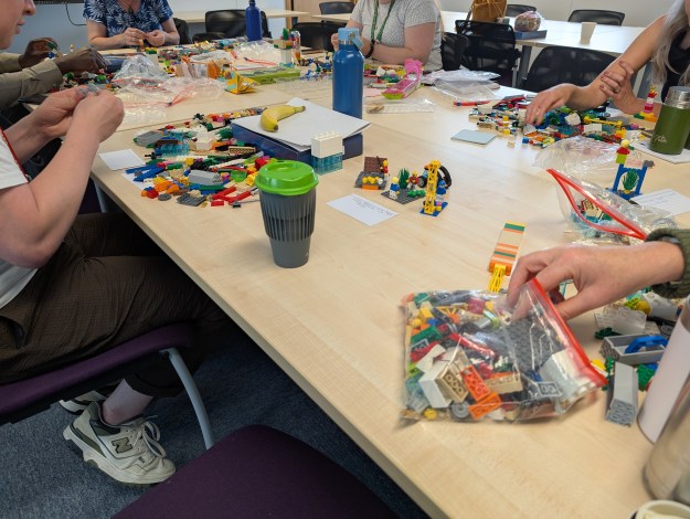 A table filled with Lego and models and surrounded by people